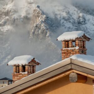two brick chimneys covered with snow with a mountain in the background