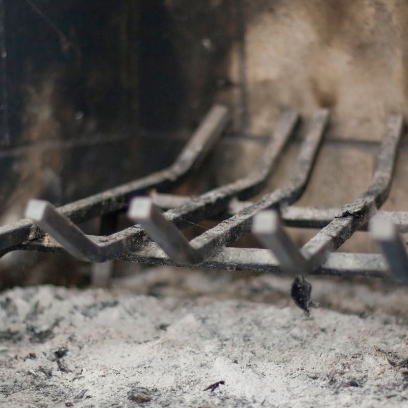 a fireplace grate in a firebox with ash underneath it